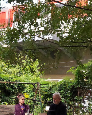 Kolja Nixdorf liest, Oda Sajouz sitzt neben ihm und auf der Hochtrasse fährt ein Regionalzug vorbei