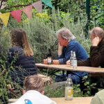 Im Garten sitzen mehrere Personen und hören konzentriert der Lesung zu.