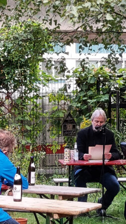 Kolja Nixdorf sitzt im Garten der Kulturfabrik Moabit und liest eine Geschichte vor